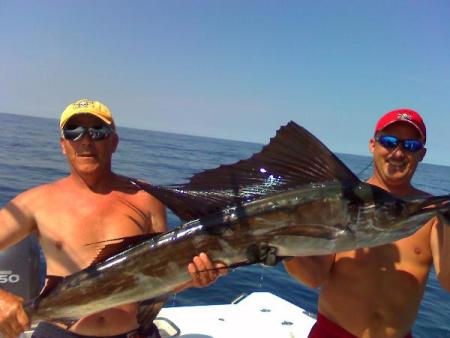 Two men holding a large marlin on a boat.