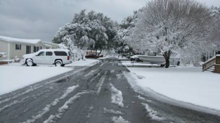 Snow-covered street with a car and boat.
