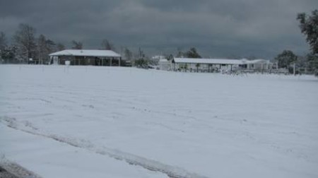 Snow-covered field with houses in the distance.