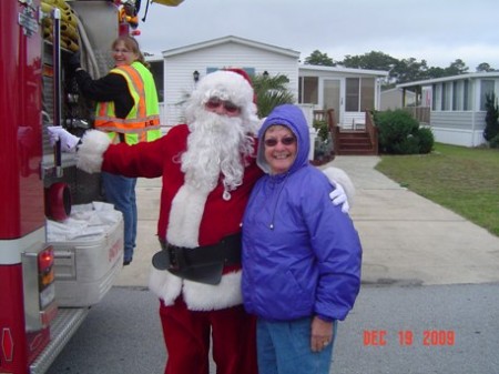Santa Claus poses with a woman and a firetruck.