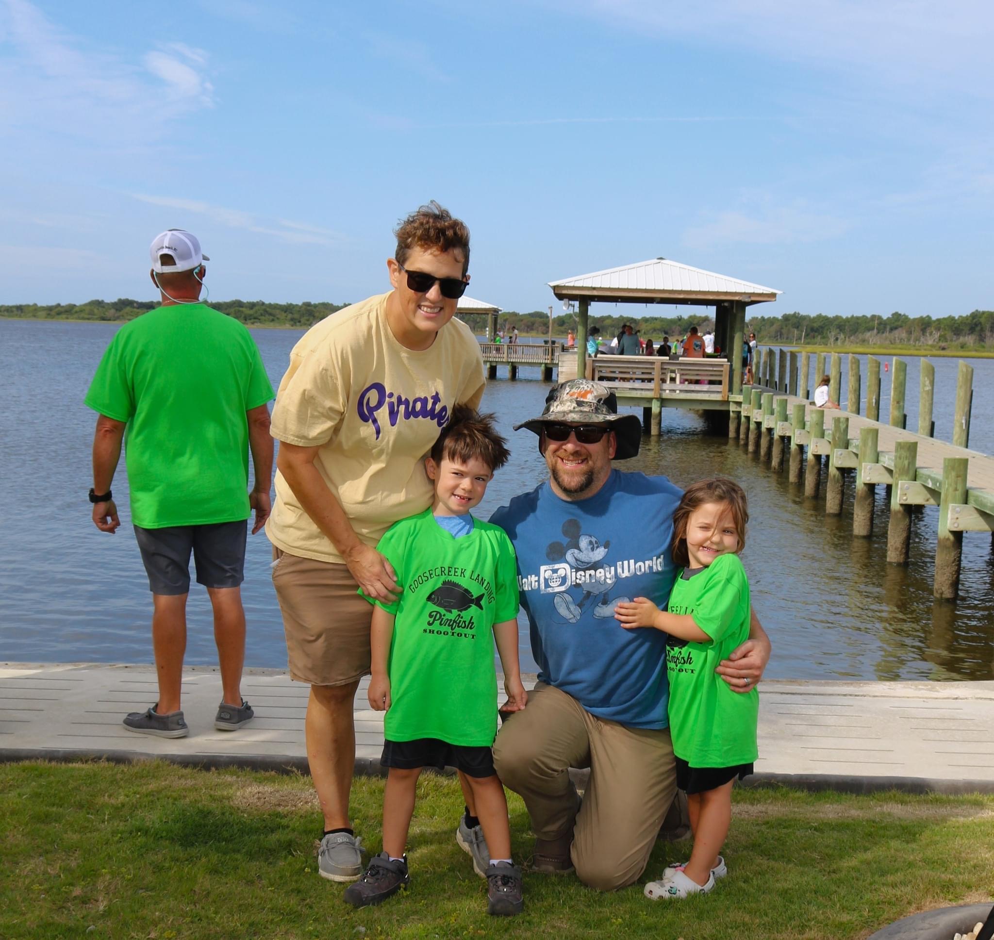 Family posing on a pier by the water.