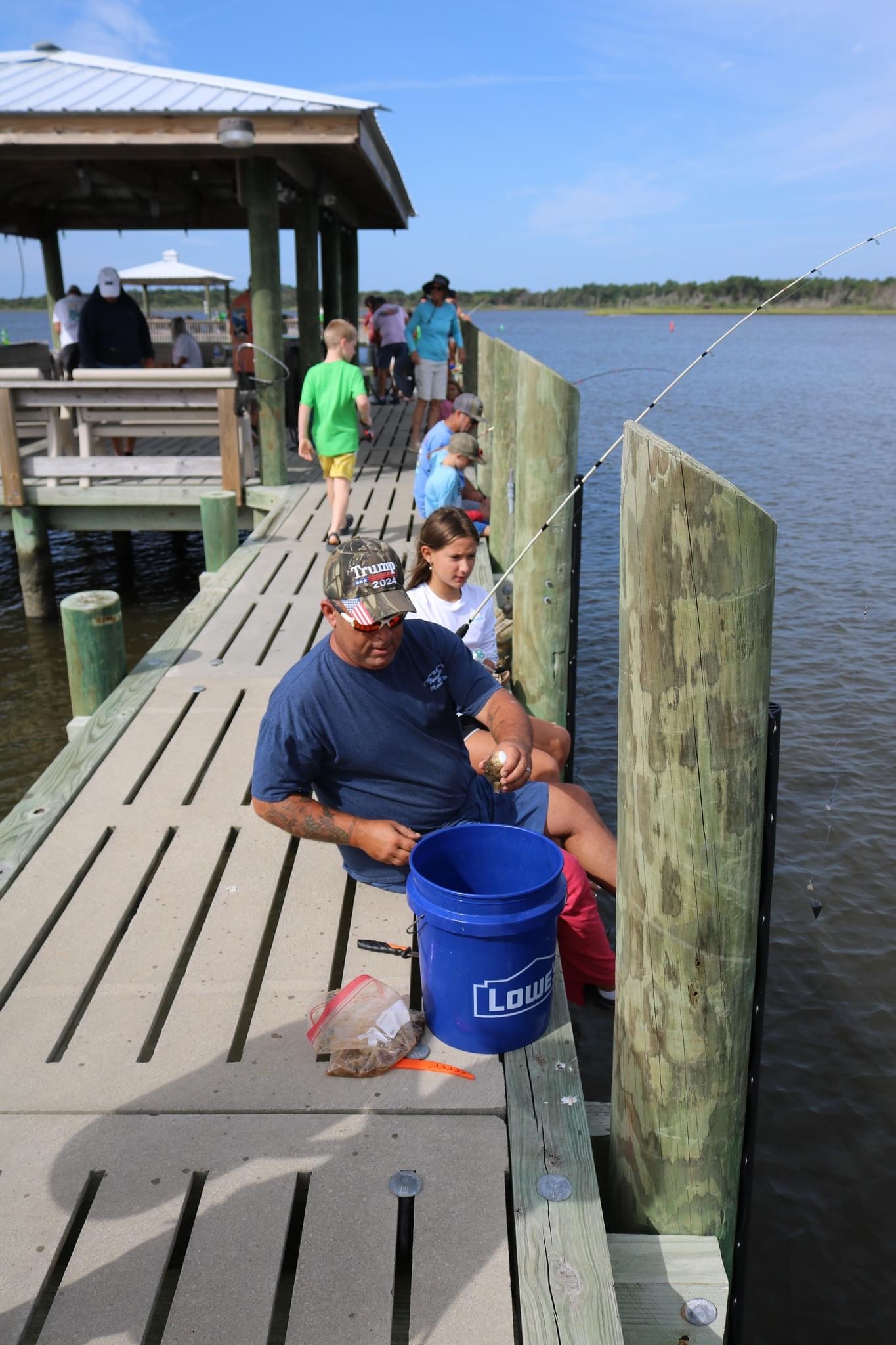 Man fishing on wooden pier with blue bucket.